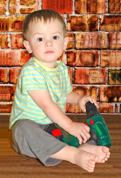 Chlapec sedí s vrtačkou na pozadí cihlová zeď — Stock fotografie