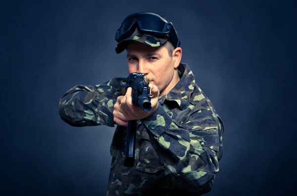 Soldado apontando uma metralhadora em um fundo azul com foco na máquina de barril — Fotografia de Stock
