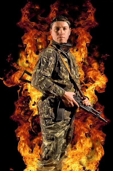 A soldier stands with a gun in his hand and safety glasses in a burning fire