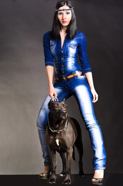 Hermosa mujer en ropa de mezclilla de pie junto a un perro — Foto de Stock
