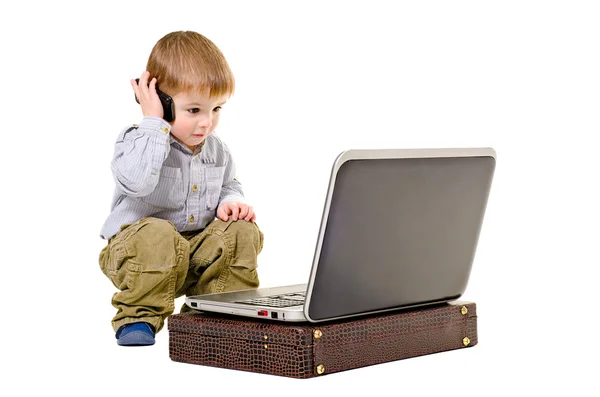 Menino bonito fala em um telefone celular olhando para laptop — Fotografia de Stock