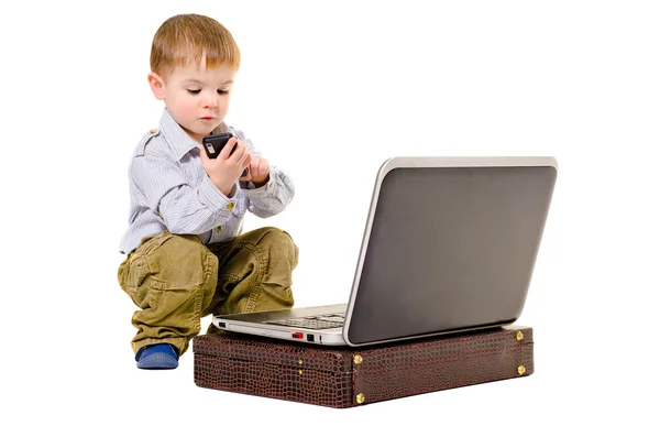 Lindo niño marca en un teléfono móvil mientras está sentado al lado de la computadora portátil —  Fotos de Stock