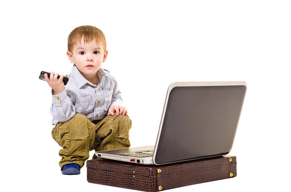 Piękny chłopiec z telefonu komórkowego jest siedząc przy laptopie — Zdjęcie stockowe