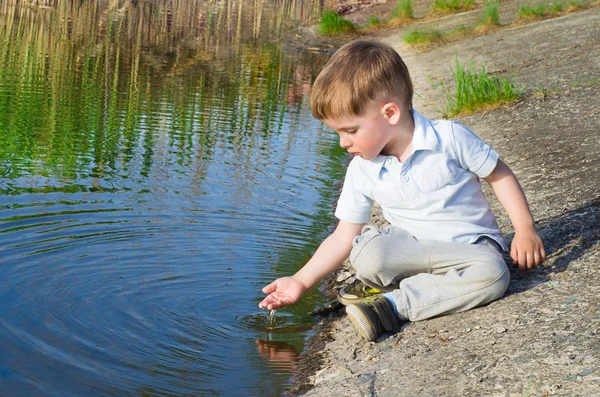 Маленький красивий хлопчик п'є воду з долоні на річці — стокове фото