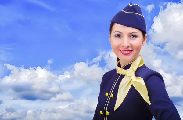Hermosa azafata sonriente en uniforme sobre un cielo de fondo —  Fotos de Stock