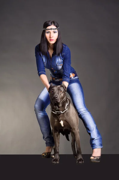 Mooie jonge vrouw in jeans kleding permanent naast een pitbulls — Stockfoto