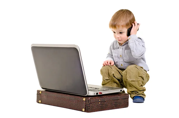Симпатичный мальчик говорит по мобильному телефону, глядя на ноутбук — стоковое фото
