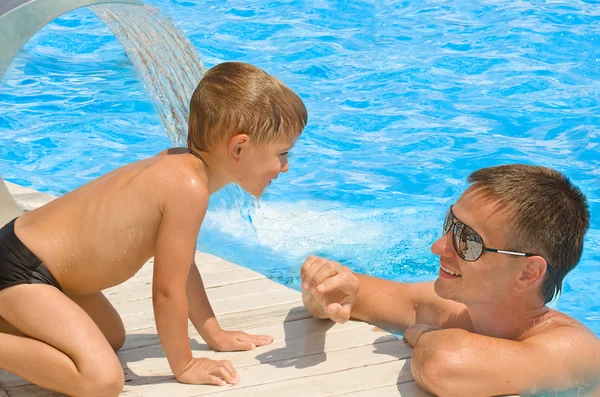 Far og søn hviler sammen ved poolen. - Stock-foto