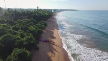 Okyanus kıyısı şafakta. Mavi su, dalgalar ve güzel plaj. Cennet dinleniyor ve denizde dinleniyor. Sri Lanka, Asya. Sahilde uzun bir uçuş. Hava 4K