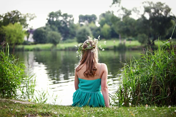 Девушка в венке, сидящая на берегу реки — стоковое фото