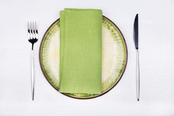 Serving - fork, knife and green napkin on green plate, top view