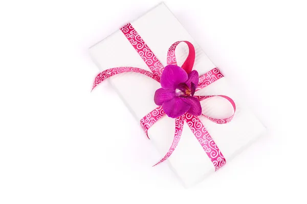 Caja de regalo con cinta rosa y orquídea púrpura sobre fondo blanco —  Fotos de Stock
