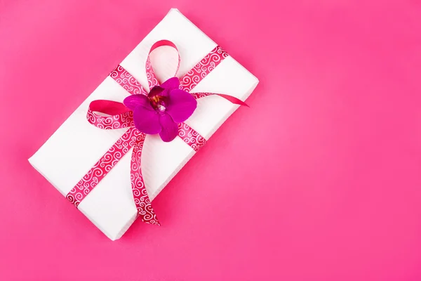 Caja de regalo con cinta rosa y orquídea púrpura sobre fondo rosa —  Fotos de Stock