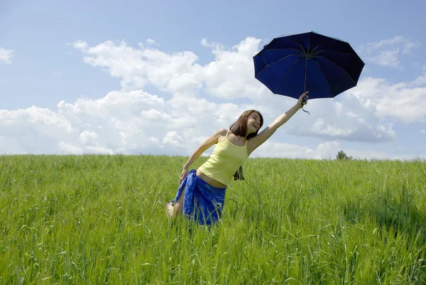 Hermosa mujer sosteniendo paraguas azul en campo de hierba verde y cielo nublado — Foto de Stock