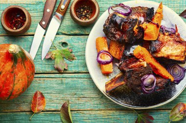 Biftek kaburgaları, ahşap zemin üzerinde balkabağı dilimleri ile fırında biftek eti.