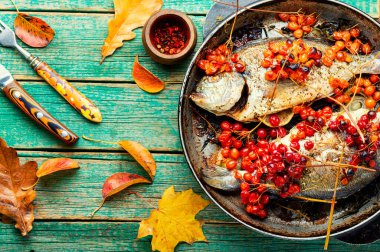 Sonbahar meyveli ızgara dorado. Tahta yüzeyde viburum ile kızartılmış balık.