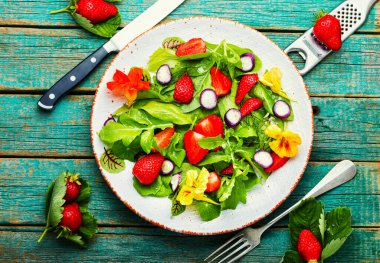Çilekli vitamin salatası, ıspanak, nasturtium ve roka. Yeşil vejetaryen salatası. Tahta masa manzaralı.