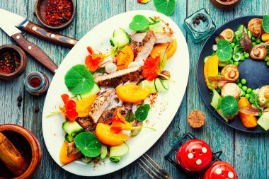 Dilimlenmiş biftek, sebze garnitürlü ve çiçeklerle süslenmiş..