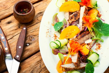 Nasturtium çiçekleriyle süslenmiş et. Dilimlenmiş domuz eti, salata..