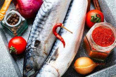 Mutfak masasında çiğ uskumru balığı ve baharat var. Pişmemiş balık