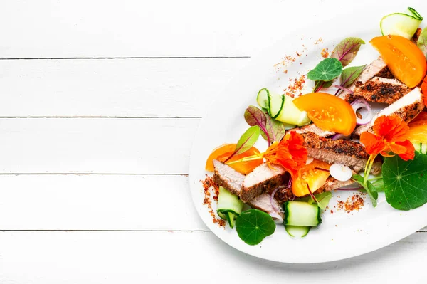 Sliced grilled steak with vegetable garnish and garnished with flowers. Meat salad, space for text