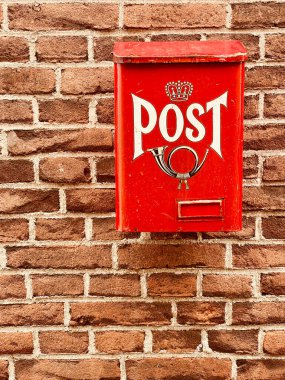 Traditional old bright red metal post box with word and picture of horn, old brick wall of the home. Postal service posting mail letters and small packages in the Dutch town of Dordrecht in Holland, the Netherlands. Conceptual concept and copy space.