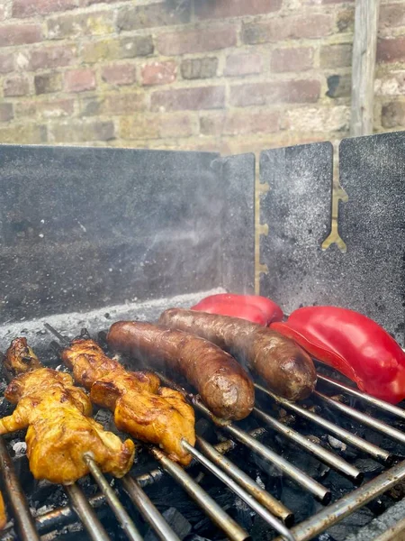 BBQ food sizzling on a smokey grill, sausages, chicken satay and red bell pepper barbecue cooking. — Stock Photo, Image