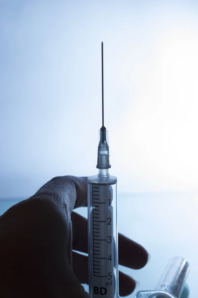 Medical syringe on gradient background with hand — Stock Photo, Image