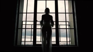 Sıska kız pencerenin önünde duruyor ve bornozunu çıkarıyor, kadın silueti, ağır çekim