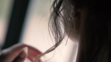 Kız saçını düzleştiriyor, yüzü görünmüyor, kulağında küpe var, güzel bir yakın plan.