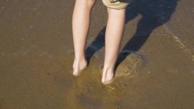 Çocuk denizde duruyor, ayakları yakın kumlu kumsalda, ayakları kumsalda ve suda, güneşli bir günde.