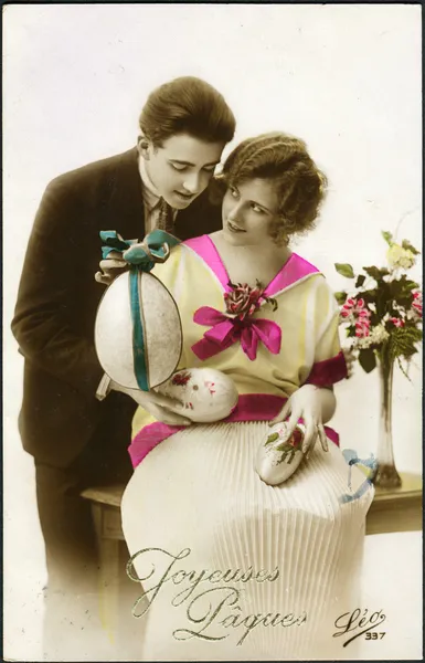 Carte postale allemande. Représente un homme et une femme, des œufs de Pâques et un bouquet de belles fleurs, vers 1923. Texte en français : Le Christ ressuscité ! — Photo