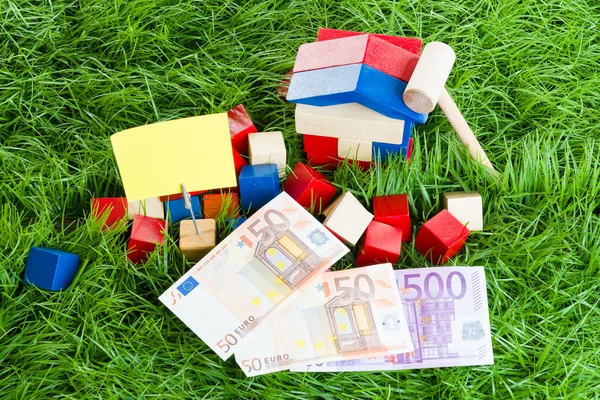 Small house of children's blocks, the money lying in the grass.