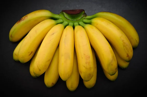 Ripe and natural looking small bananas on dark background.