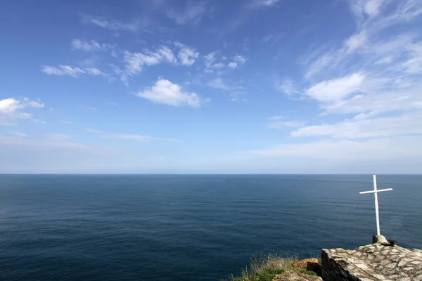 Cruz branca contra o mar, céu azul e nuvens fofas — Fotografia de Stock