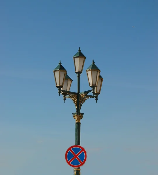 Old street light with road sign abainst blue sky — Stock Photo, Image