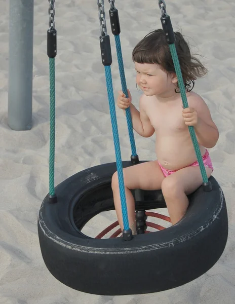 Retrato de una hermosa niña en el columpio de un neumático viejo — Foto de Stock