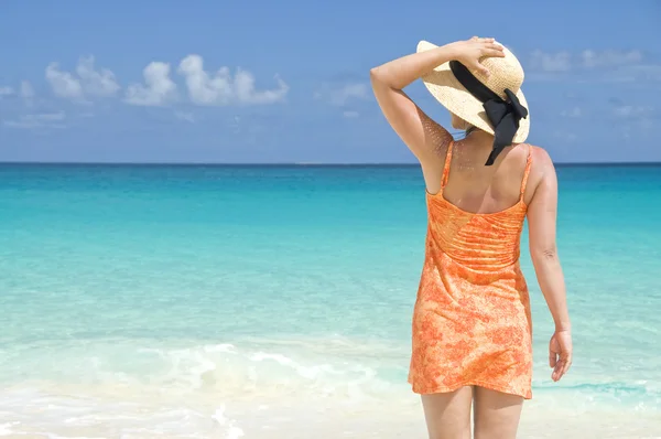 Žena v oranžové šaty a slaměný klobouk na pláži — Stock fotografie