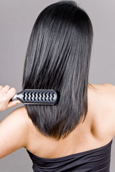 Vrouw haar lange rechte zwarte haren borstelen — Stockfoto