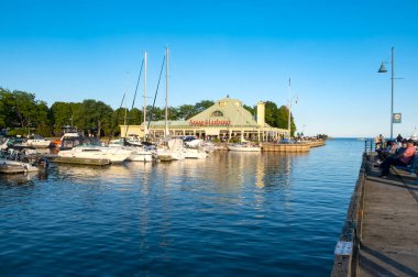 Mississauga, Ontario - August 28, 2022: Parked Boats and Yachts at the Port Credit Marina in Front of the Snug Harbour Restaurant Filled with Patrons on a Summer Evening