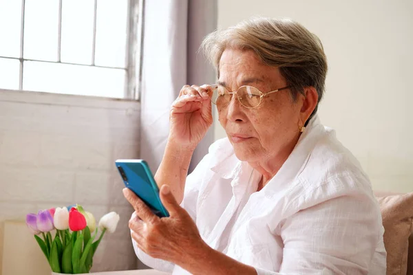 白髪のアジア系の高齢女性が携帯電話を使って眼鏡をかけている 高齢者の目の問題 ぼやけたビジョン ストックフォト