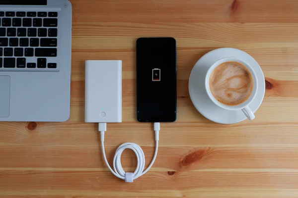 Plug in USB charger from powerbank input mobile phone or smartphone and laptop computer and coffee cup cappuccino on wooden floor,Top view.