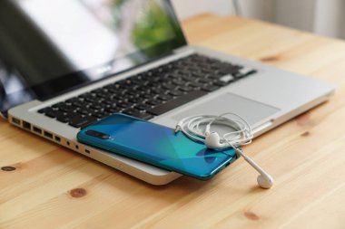 Laptop bilgisayarında akıllı telefon ve kulaklıklar, ahşap arka planda günlük kullanım için elektronik cihazlar..