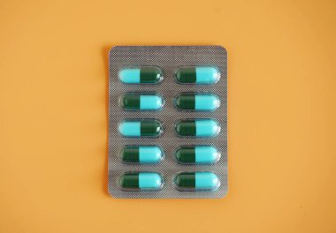 Turuncu arka planda mavi-yeşil kapsül hap paneli. Amoksisilin bir penisilin antibiyotiğidir. Bakterilerin neden olduğu enfeksiyonları tedavi etmek için kullanılır.