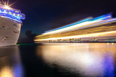 Nassau, Bahamalar - 22 Haziran 2019: Denizcilik gemisinin Mariner 'ı gece Prens George Rıhtımı' ndan ayrılırken ve ışık izleri bırakırken çekildi. Karnaval Özgürlük ön planda. Uzun pozlama.
