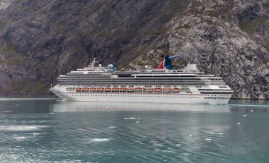 Alaska, USA - September 1 , 2018: Carnival Splendor sailing in one of the Alaskan Fjords. Beautiful turquoise icy water in the foreground, massive mountain in the backgorund. clipart