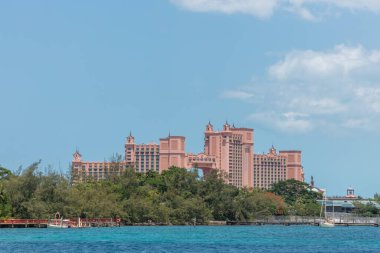 Nassau, Bahamalar - 14 Mayıs 2019 Atlantis Cennet Adası 'ndaki tatil köyü ve otelden uzak çekim. Ön planda turkuaz su ve ağaçlar var. Arka planda mavi bulutlu gökyüzü.