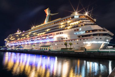 Nassau, Bahamalar - 16 Haziran 2019: Karnaval Liberty yolcu gemisinin güzel alçak açılı çekimi Prens George Wharf 'a gece yanaştı. Ön plandaki liman suyundaki muhteşem ışık yansımaları..