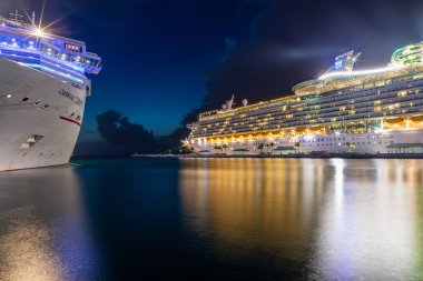 Nassau, Bahamalar - 6 Temmuz 2019: Denizlerin Denizcisi 'nin Prens George Wharf' tan gece ayrılıp suda yansımalarını bıraktığı güzel bir sahne. Karnaval Özgürlüğü ön planda.