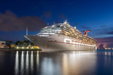 Nassau, Bahamalar - 24 Ağustos 2019: Karnaval Özgürlük yolcu gemisi Prens George Wharf 'a yanaştı. Mavi saat. Geminin ve limanın ışıklarının ön plandaki liman suyundaki muhteşem yansımaları..